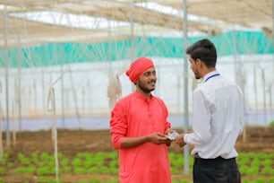 Joven banquero indio dando dinero a agricultor en invernadero