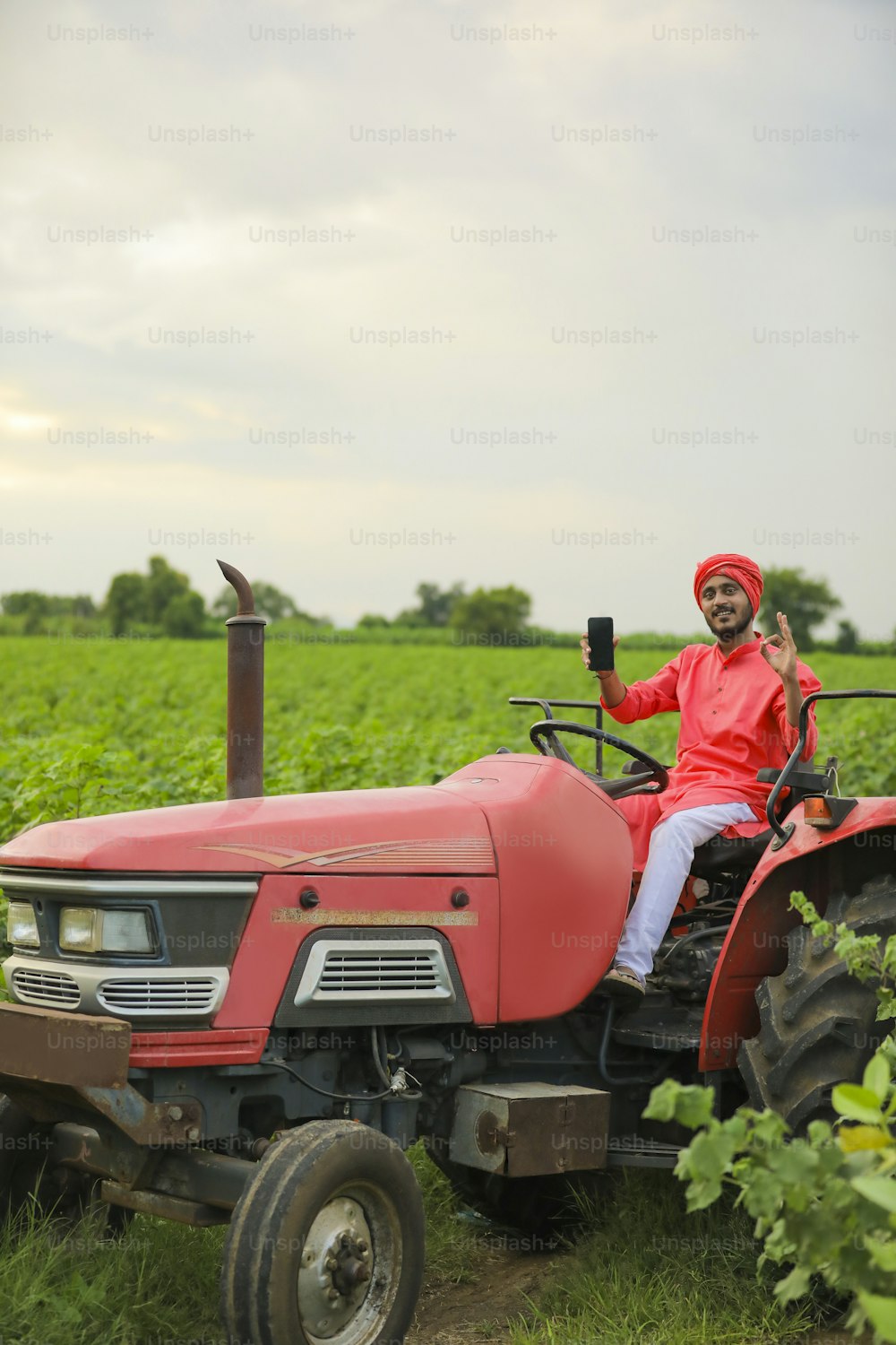 Joven agricultor indio mostrando teléfono inteligente o tableta en tractor