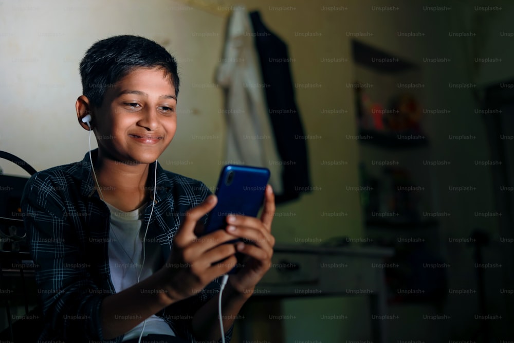 Lindo niño indio usando teléfono inteligente y auriculares gadget.