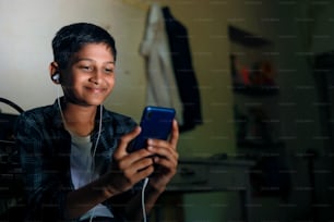 Bambino indiano sveglio che utilizza il gadget per smartphone e cuffie.