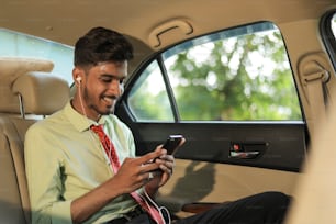 Junger indischer Mann, der im Auto Musik auf dem Handy hört