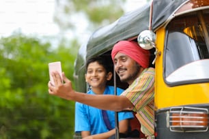 Conductor indio de auto rikshaw o tuk tuk tomándose selfie con su colegial