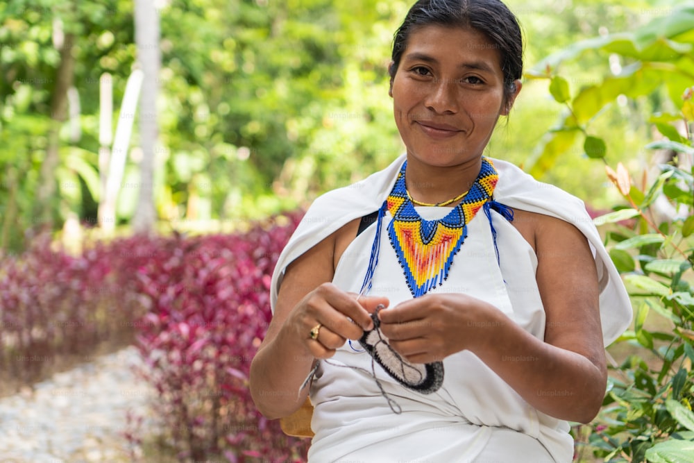 Indigenous woman in traditional clothing weaving looking at the camera