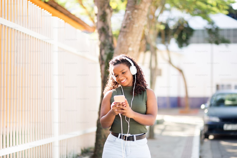 Portrait of a happy young woman listening to music via headphones on the street