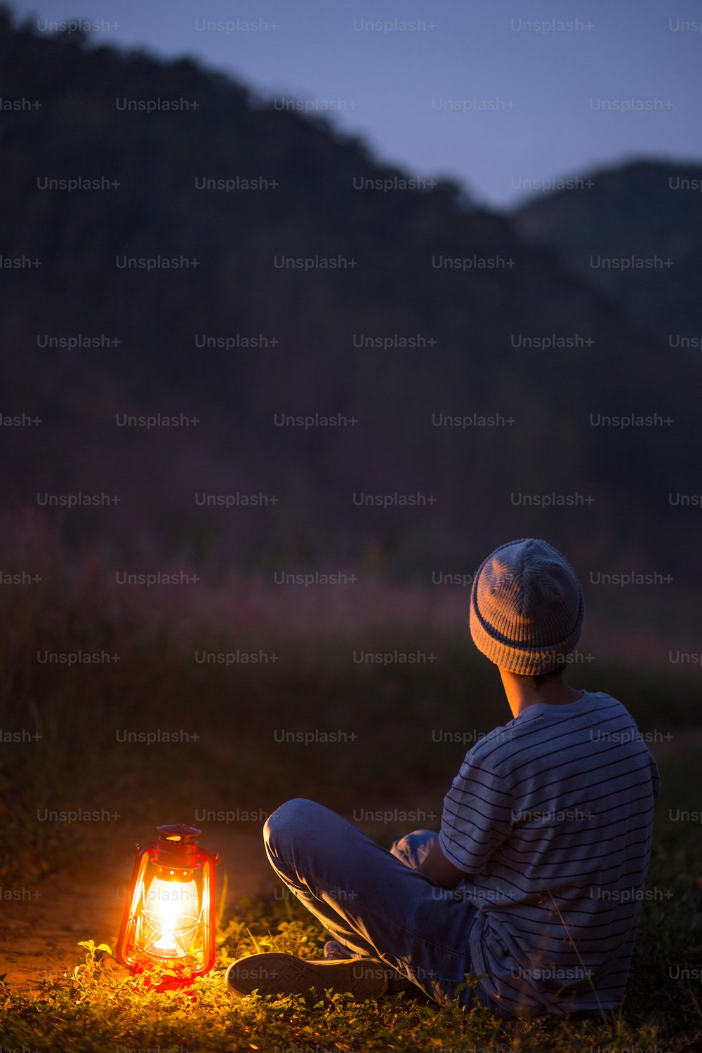 young boy sitting contemplating the nithfall with the lamp lit
