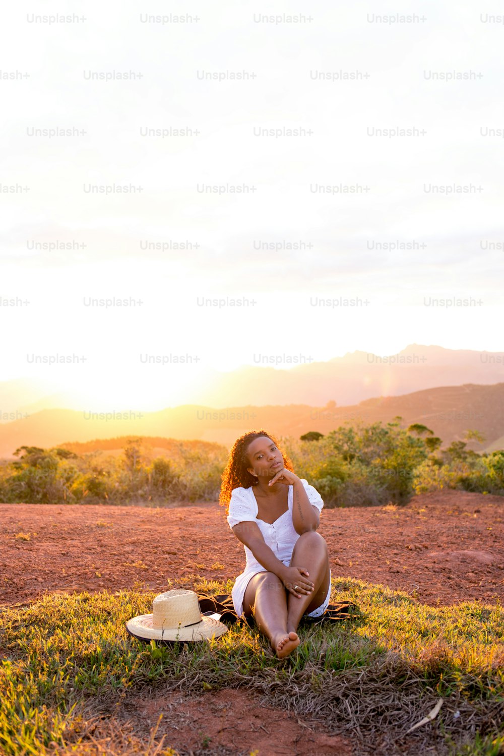 Young woman barefoot and sitting on the ground, enjoying nature, with the sunset in the background.