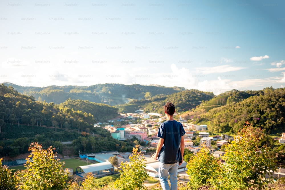 Man standing on the top of the mountain looking at the landscape with a town in the valley.