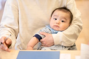 asian baby held by a mother doing desk work at home