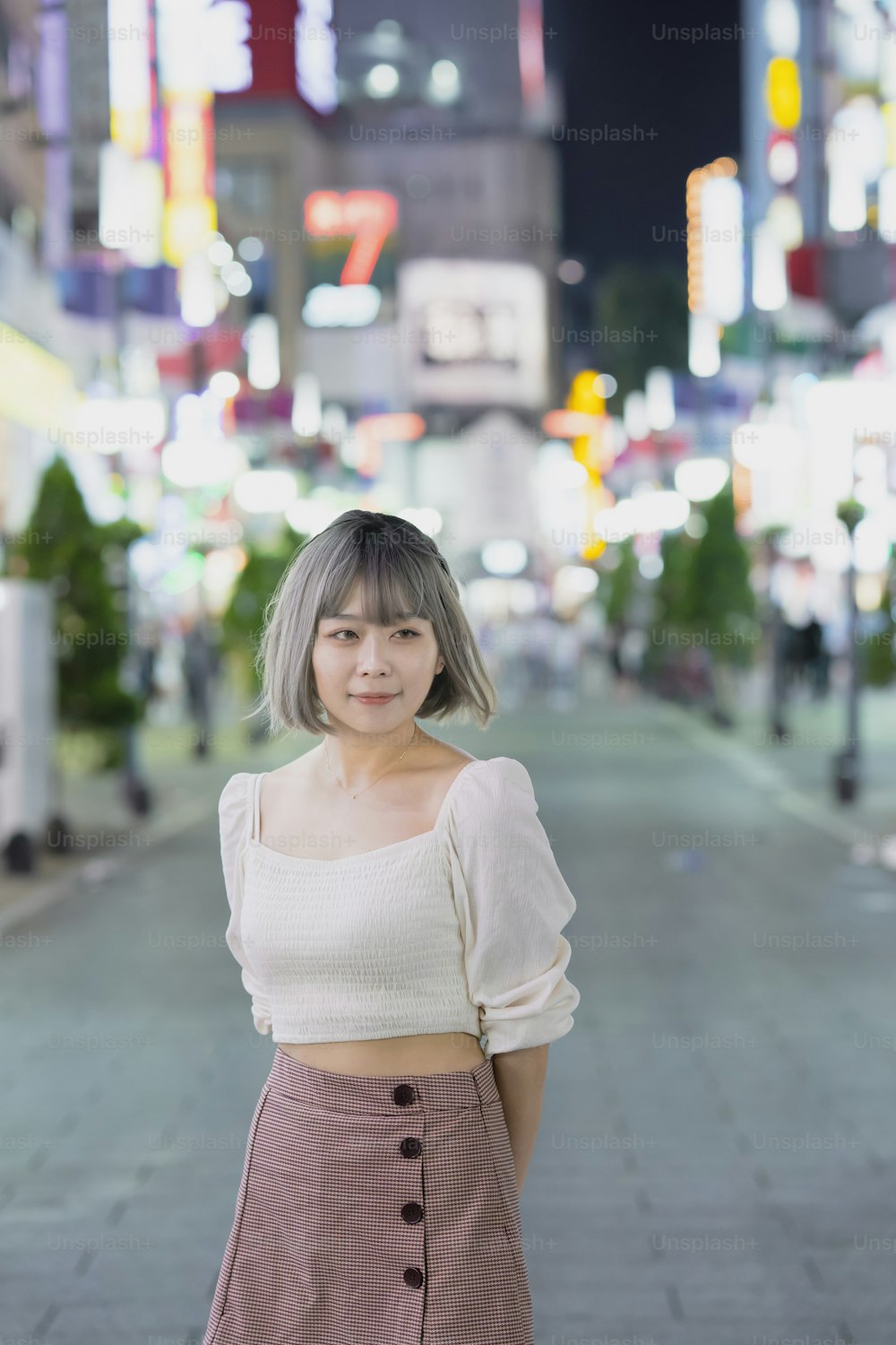 밤에 도쿄의 빛나는 도시 풍경에서 포즈를 취하는 젊은 여자