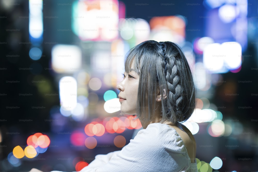 Mulher nova que posa na paisagem urbana brilhante de Tóquio à noite