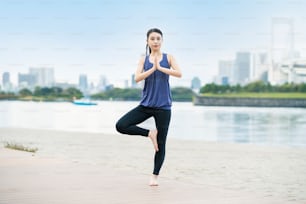 Asian young woman doing yoga on the beach in the city