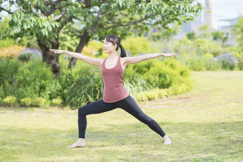 Mulher nova que faz yoga em um parque verde no dia fino