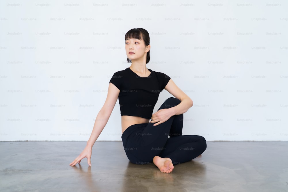 Frau sitzt und macht Yoga drinnen mit schwarzer Kleidung