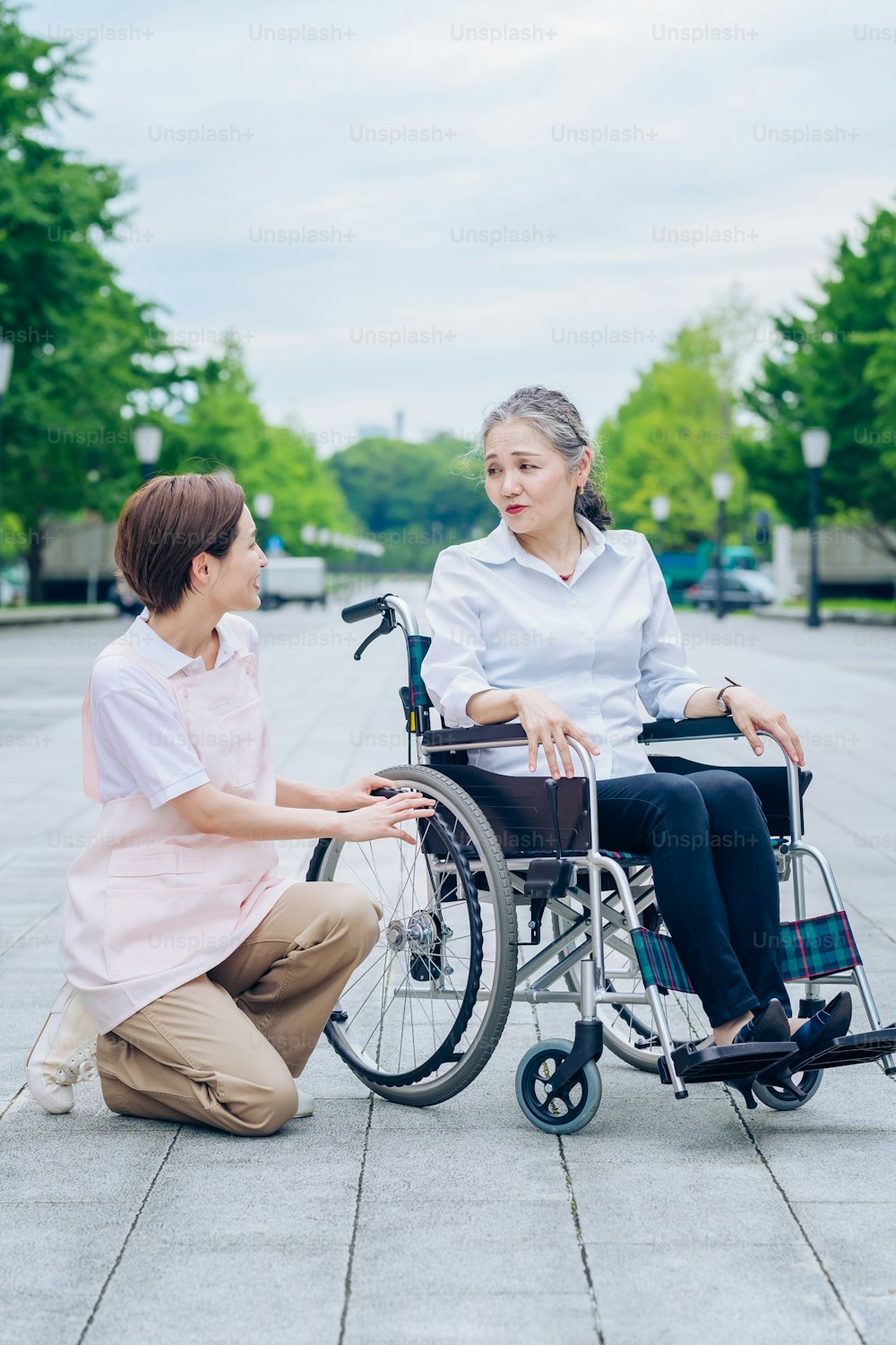 Uma mulher em uma cadeira de rodas e uma mulher em um avental cuidando dela