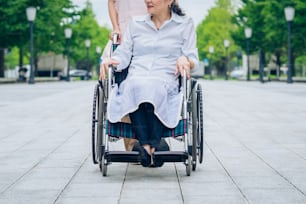 Una mujer en silla de ruedas y una mujer con delantal para cuidar al aire libre