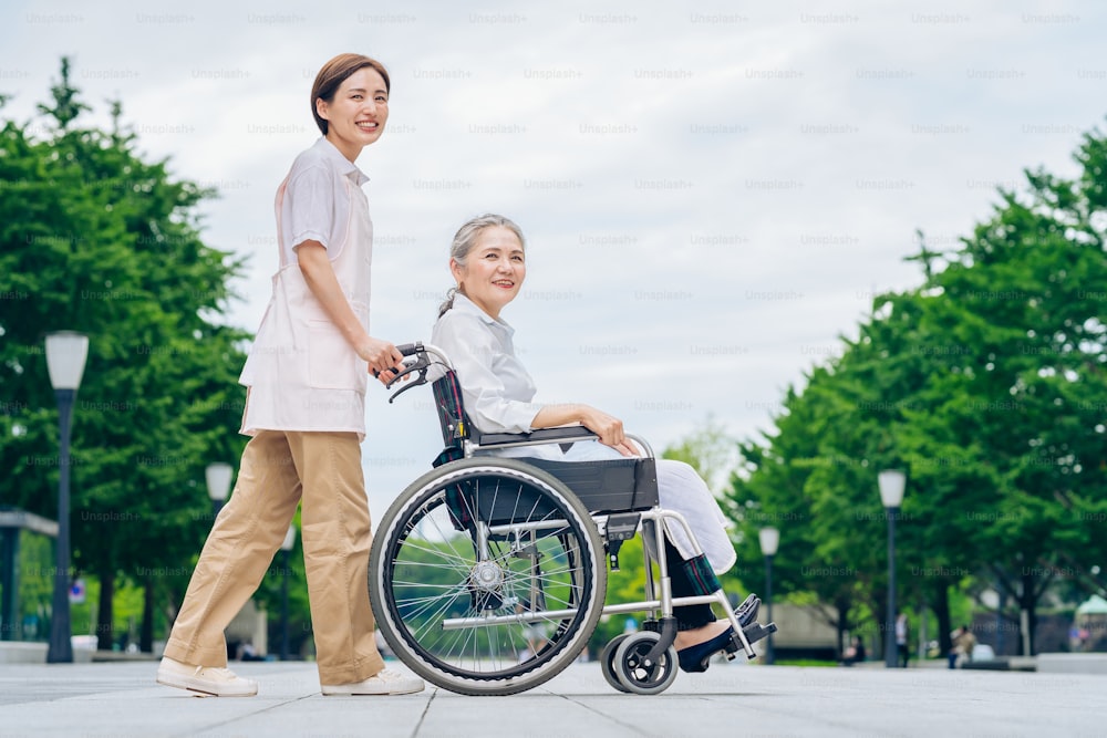 Uma mulher em uma cadeira de rodas e uma mulher jovem em um avental para cuidar ao ar livre