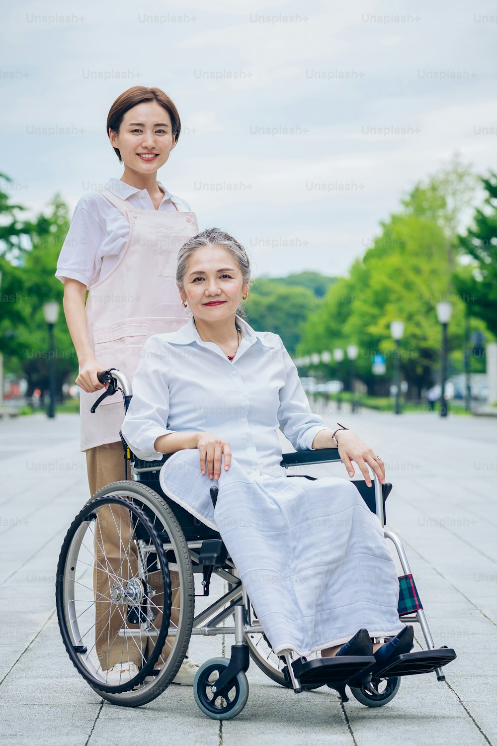 Uma mulher em uma cadeira de rodas e uma mulher jovem em um avental para cuidar ao ar livre