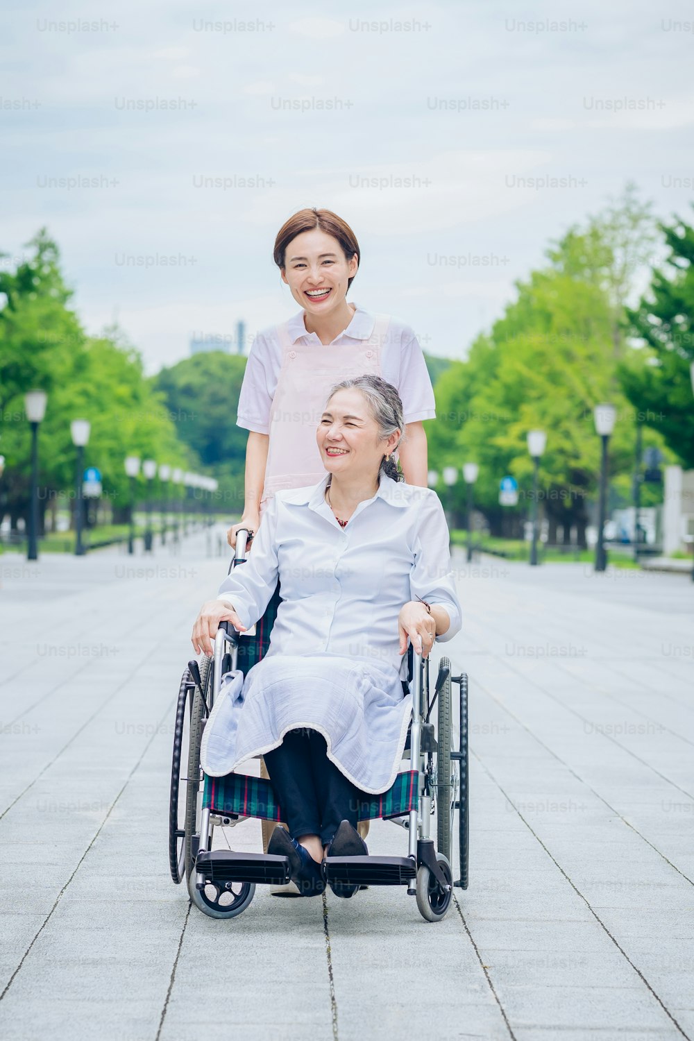 A woman in a wheelchair and young woman in an apron to care for outdoors
