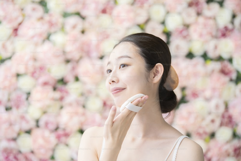 Giovane donna asiatica (giapponese) che mette il soffio alla sua pelle del viso