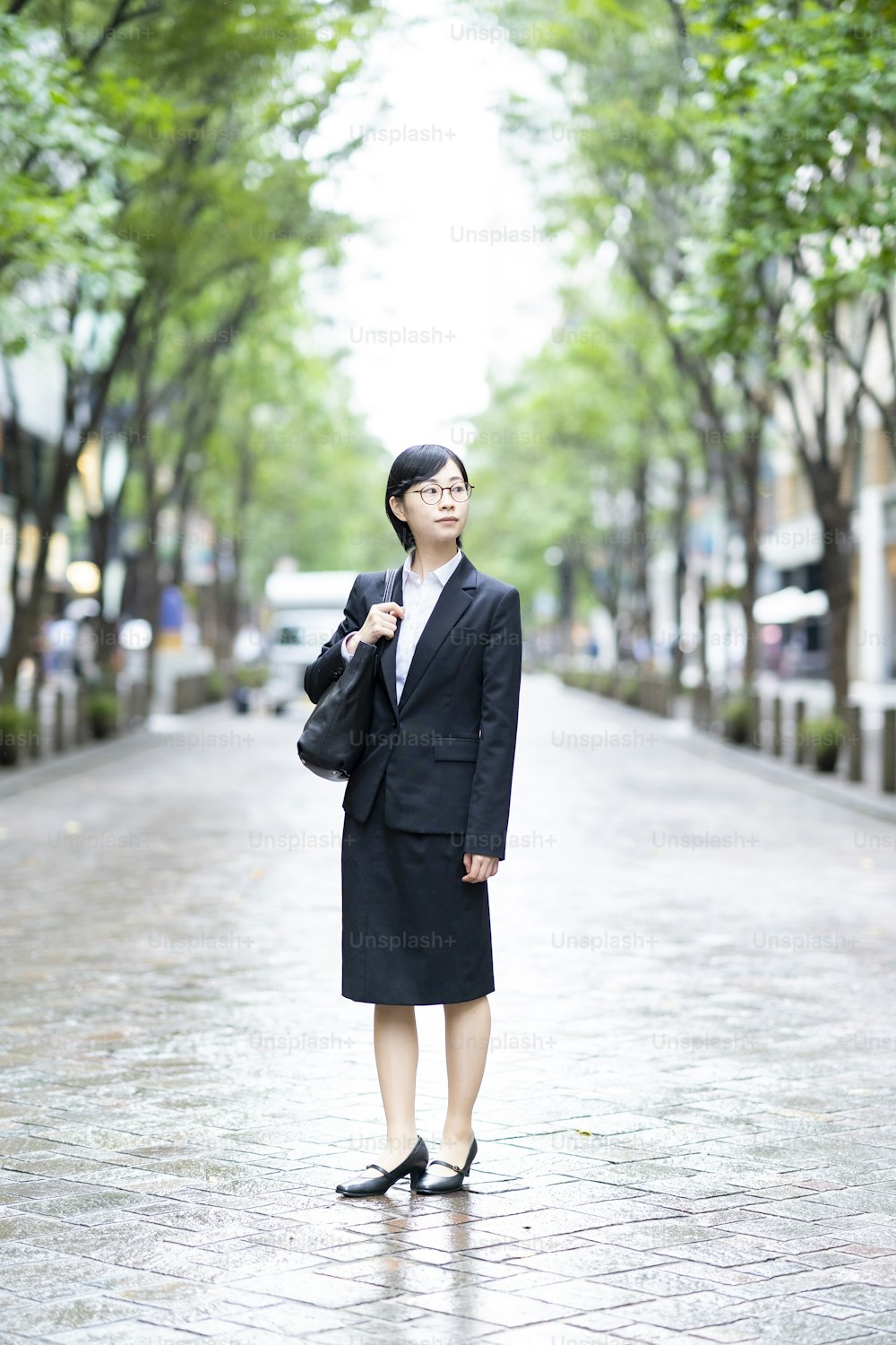 A young woman in a suit standing on a street lined with roadside trees