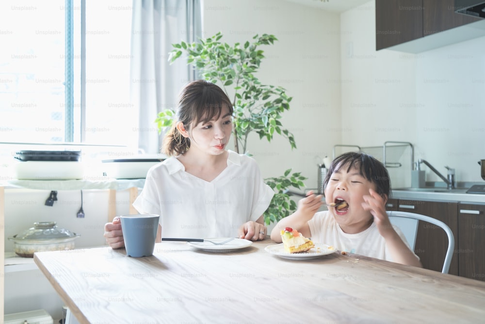Madre e hija asiáticas comiendo pastel en la mesa del comedor en casa