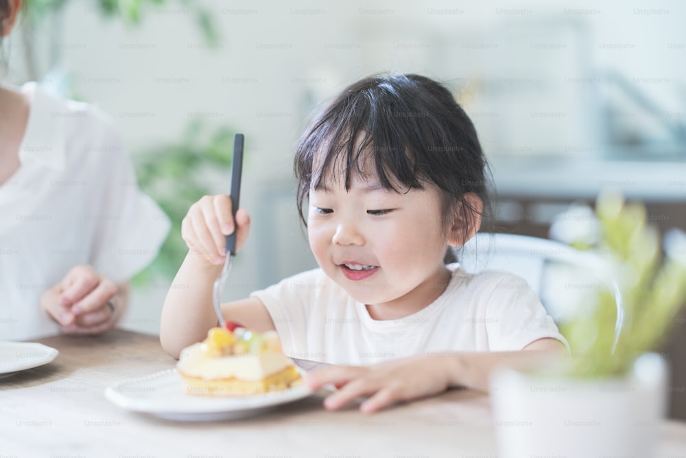 Asian mom and daughter eating cake at dining table at home