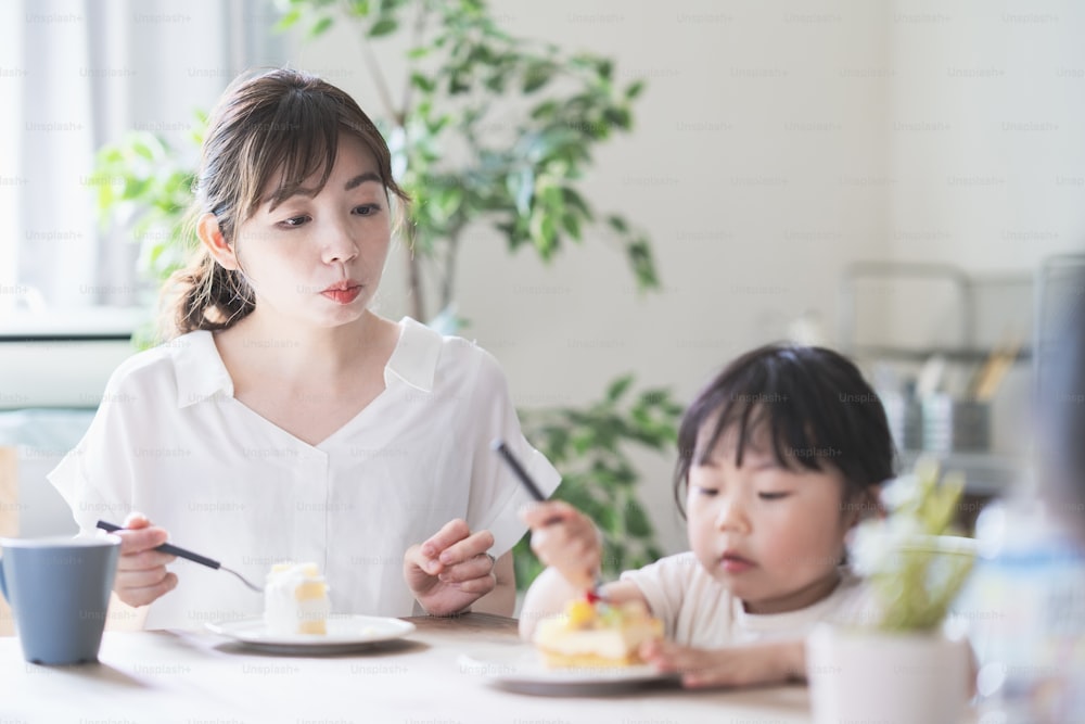 Mãe e filha asiáticas comendo bolo na mesa de jantar em casa
