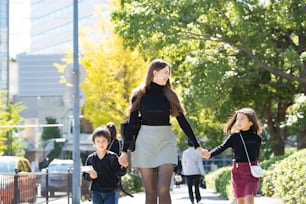 Mãe e dois filhos caminhando ao ar livre de mãos dadas com sorriso