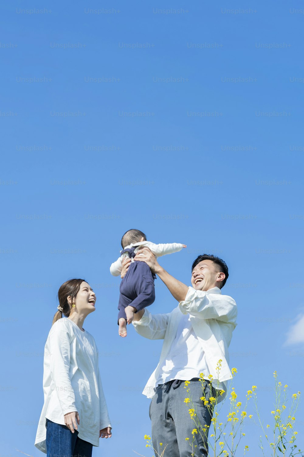 Parents holding their baby high under the blue sky