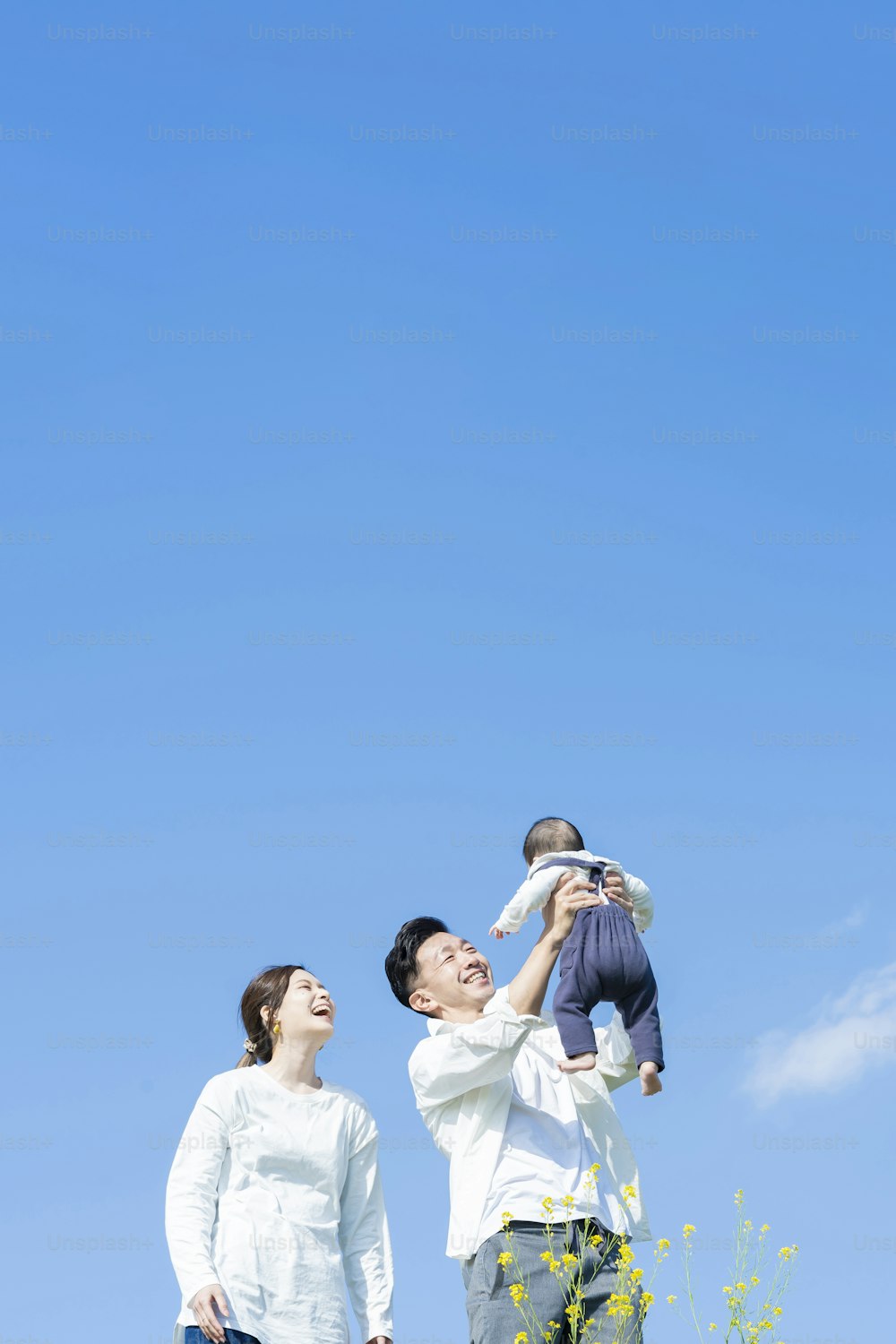 Parents holding their baby high under the blue sky