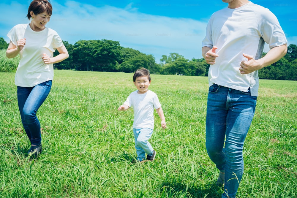 Parents and their child running around the meadow on fine day