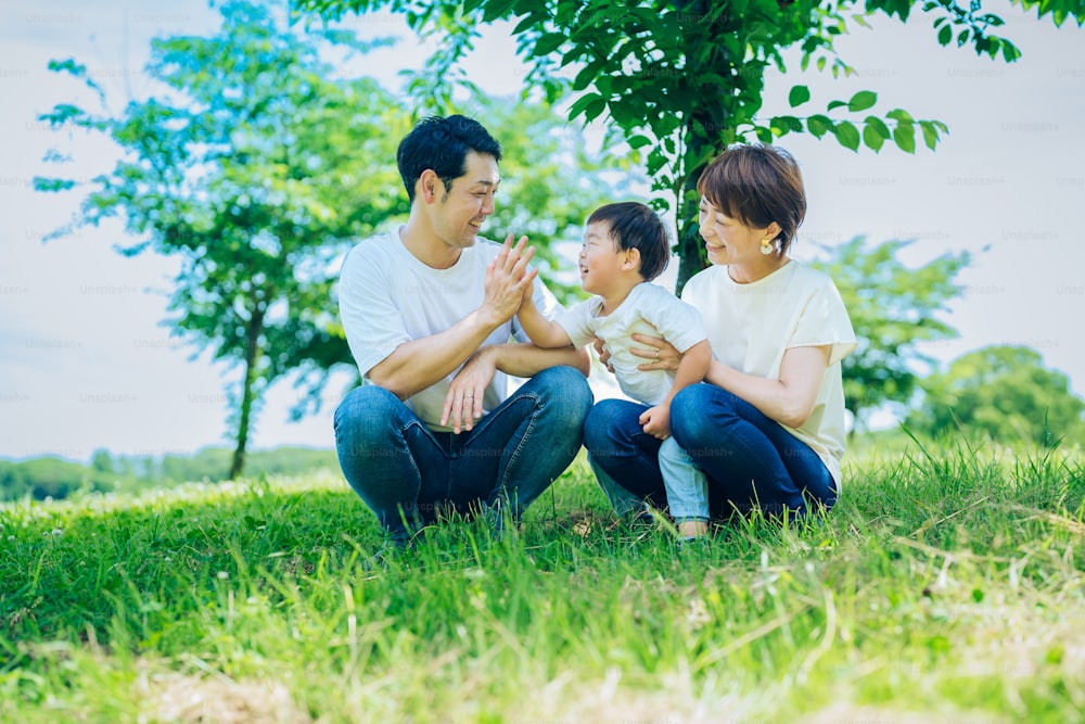 Eltern und ihr Kind sitzen an schönen Tagen auf einer sonnigen Grünfläche