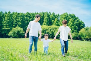 Parents and their child holding hands and walking on a sunny green space