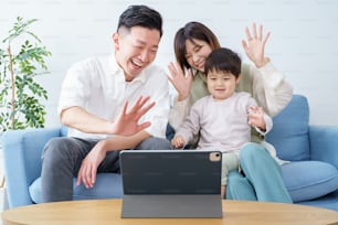Parents and their little boy waving toward the screen of a tablet PC