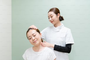 Asiatische Praktikerin massiert Schultern und Nacken einer Patientin