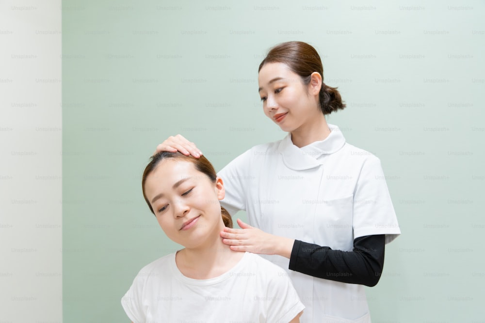 Practicante asiática masajeando hombros y cuello de paciente femenina