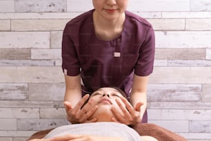 Eine weibliche Praktizierende massiert das Gesicht einer asiatischen Patientin
