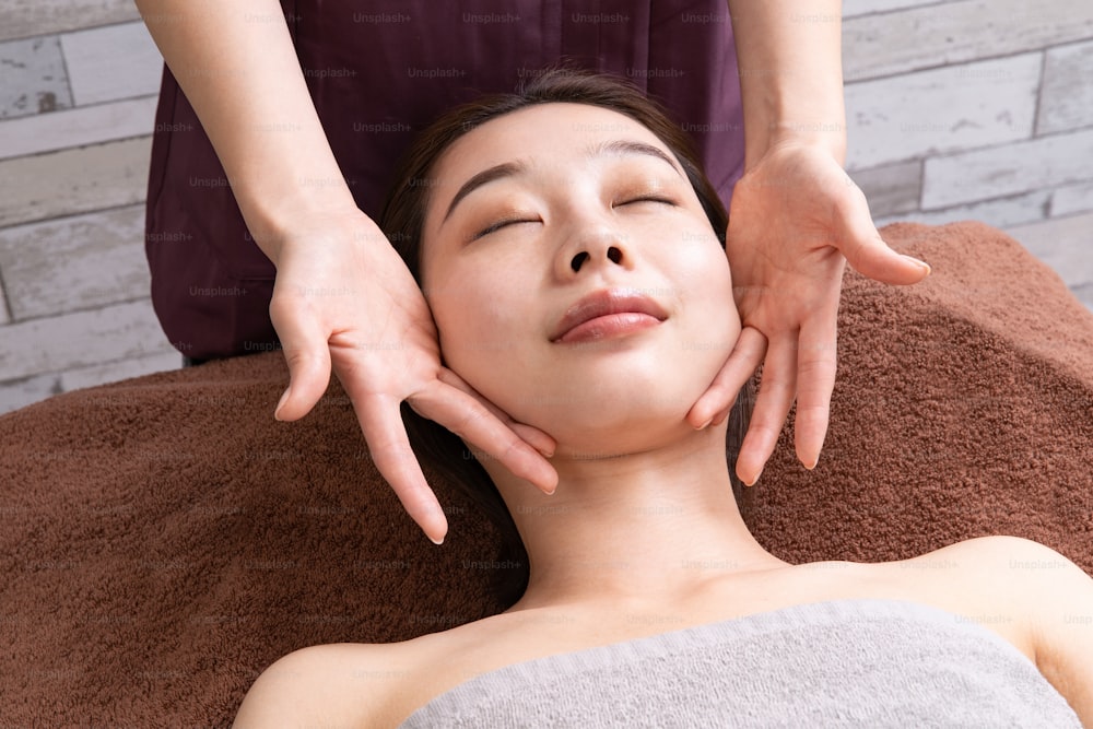 Uma praticante do sexo feminino massageando o rosto da paciente asiática do sexo feminino