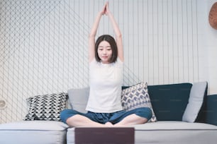 Young Asian woman taking an online yoga lesson in the living room