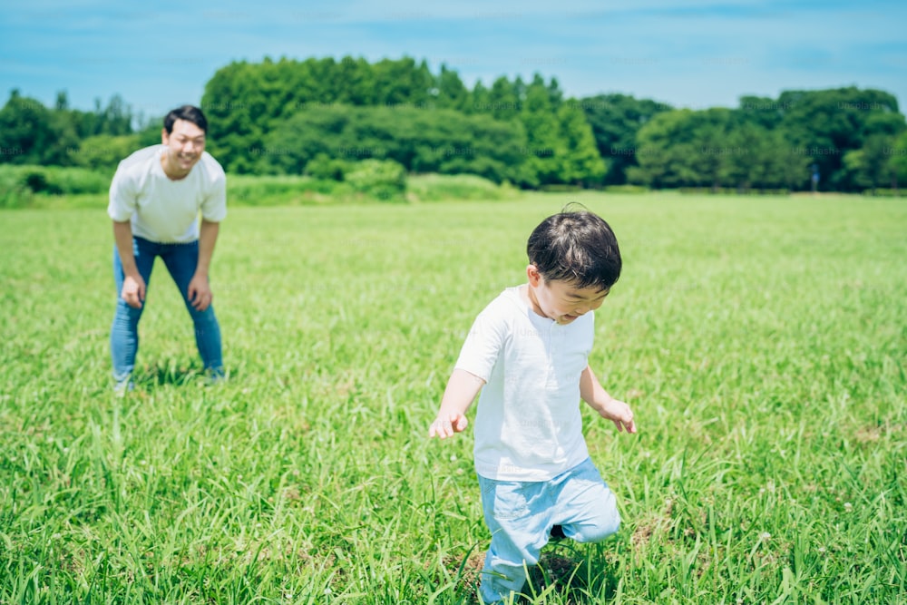 A boy running in the meadow and a father watching over on fine day