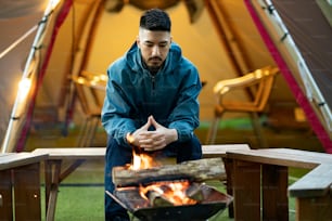 A man enjoying a bonfire in front of tent