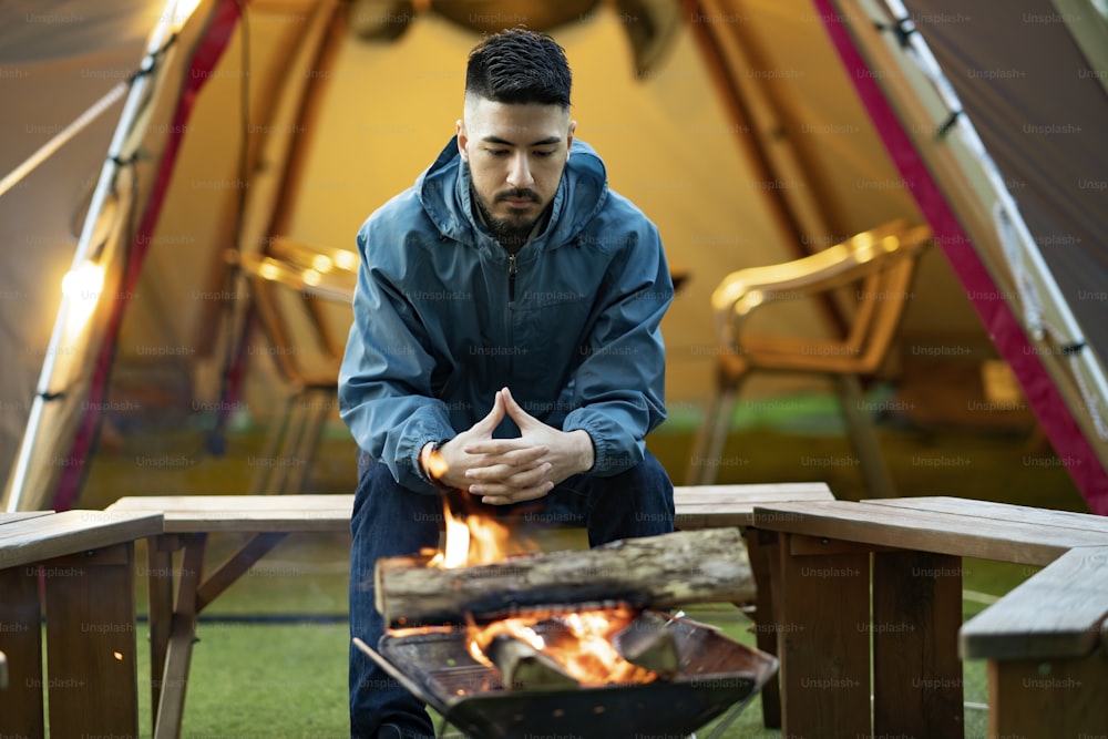 A man enjoying a bonfire in front of tent