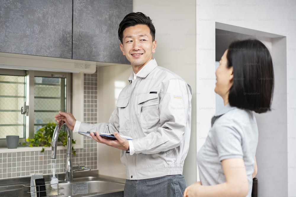 Un hombre en ropa de trabajo explicando a una mujer en la cocina (proveedor de agua)