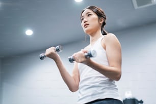 Joven asiática haciendo entrenamiento muscular con mancuernas