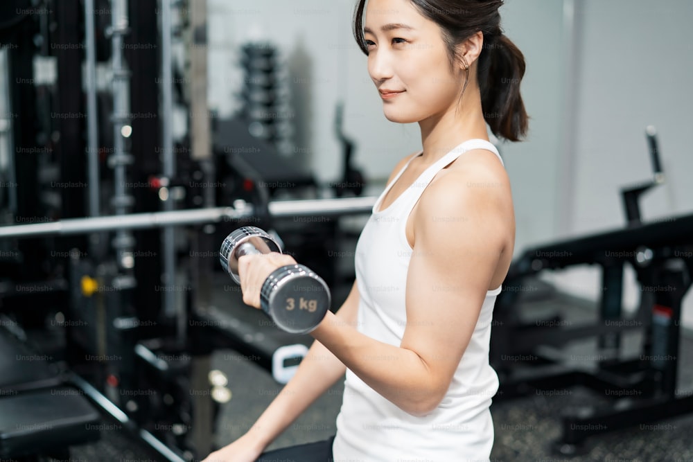 Joven asiática haciendo entrenamiento muscular con mancuernas