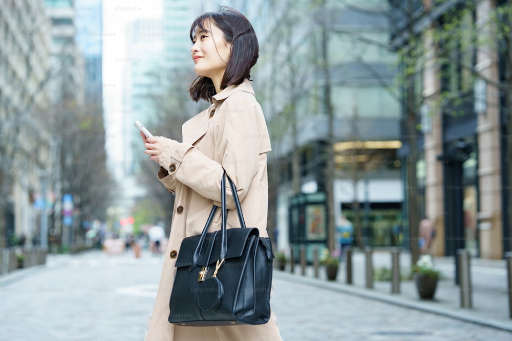 Eine Frau, die mit einem Smartphone in der Hand in einem Geschäftsviertel spazieren geht