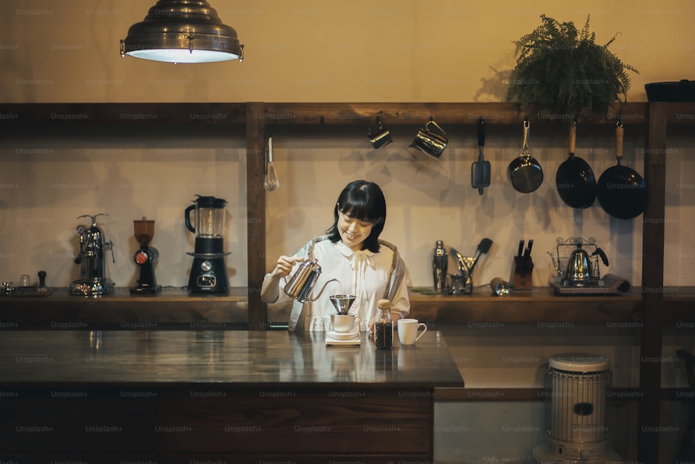 Eine junge Frau, die in einem ruhig beleuchteten Raum Kaffee mit einem Handtropfen kocht