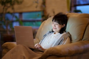Una mujer joven usando una computadora portátil en el sofá en una habitación con poca iluminación