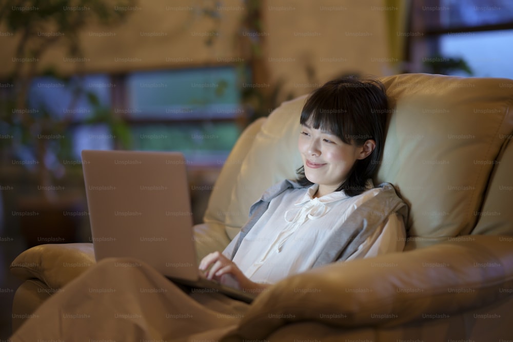 A young woman using a laptop on the sofa in a room with low lighting