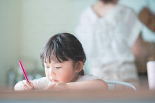 Disegno asiatico della ragazza con penne colorate al tavolo da pranzo a casa